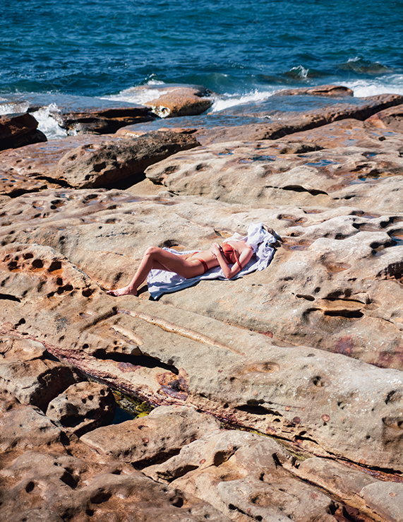 Person Sunbathing on Weathered Coastal Rock Beside the Ocean