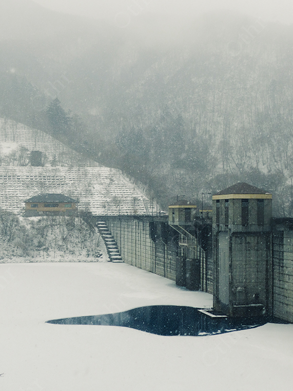 Snow-Covered Dam and Mountains in Heavy Winter Fog
