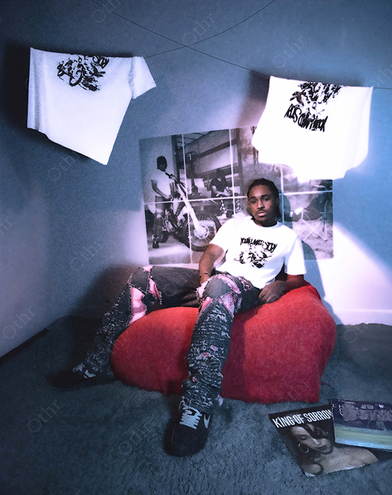 Man Reclining on Red Bean Bag Chair in Room With Hanging T-Shirts and Wall Posters Under Soft Blue Lighting