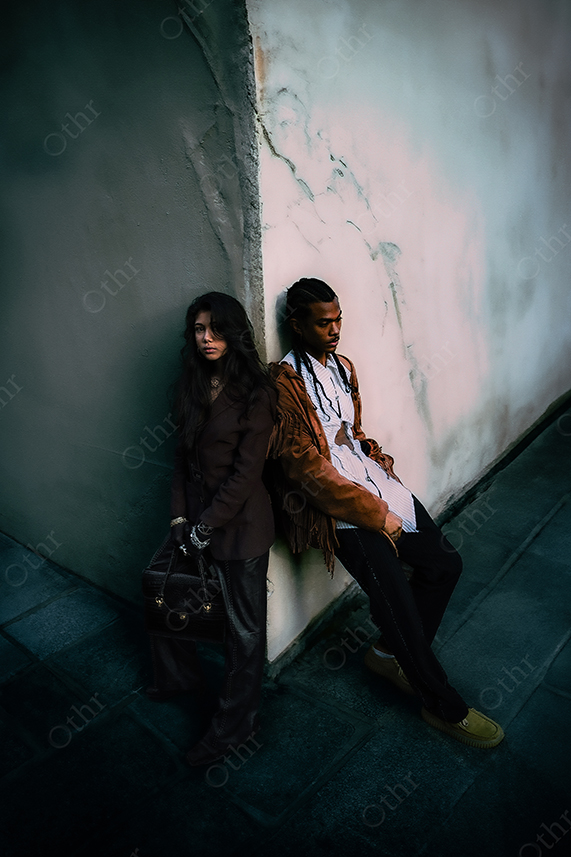 Two People Leaning Against Corner Wall in Narrow Urban Passage Under Moody Low Light