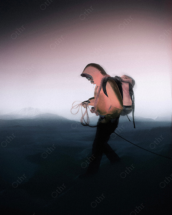 Person Walking Across Foggy Mountain Landscape Wearing Hooded Jacket and Backpack While Holding Rope