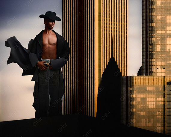 Man Wearing Wide-Brim Hat and Open Coat Standing Shirtless Against Tall City Skyscrapers at Golden Hour