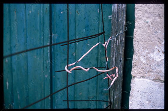 Bent Wire Tied to Rusted Rods Against Weathered Wooden Door and Stone Wall