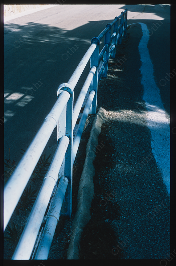 Blue Roadside Guardrail Casting Shadows Along Quiet Asphalt Street in Daylight