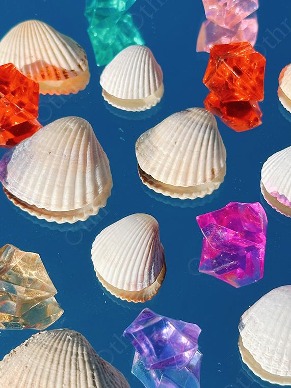White Seashells Scattered With Coloured Acrylic Crystals on Blue Reflective Background