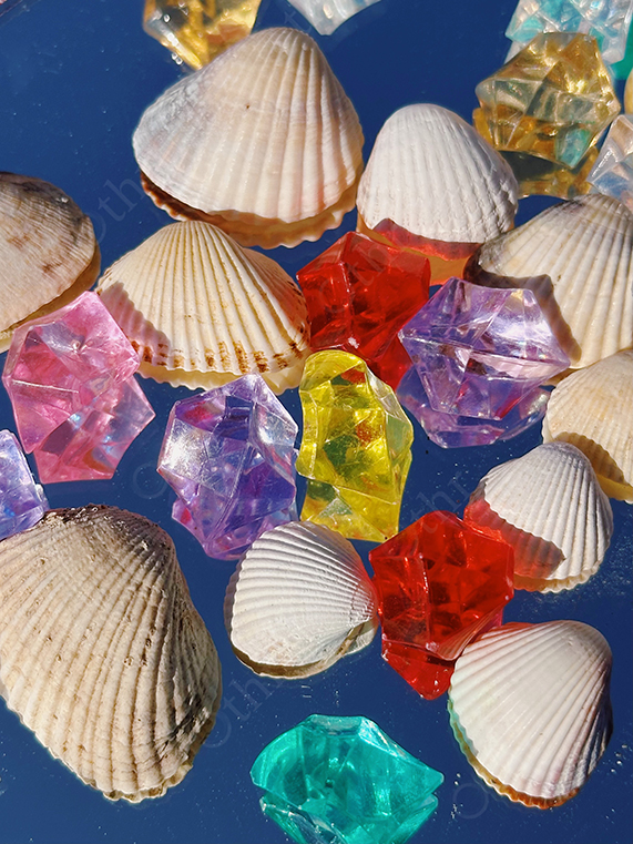 White Seashells Arranged With Multicoloured Acrylic Crystals on Blue Reflective Surface