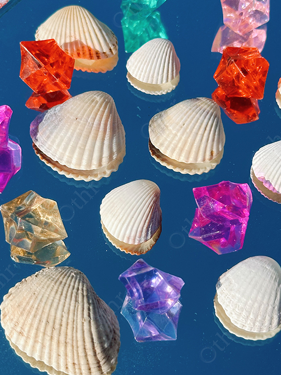 White Seashells Evenly Arranged With Coloured Acrylic Crystals on Blue Reflective Surface
