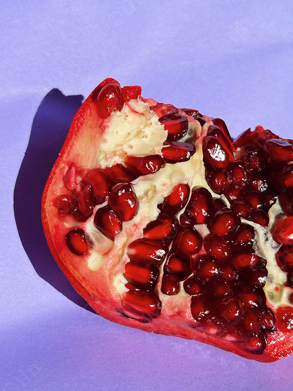 Close-Up of Cut Pomegranate With Shiny Red Seeds on Soft Purple Background