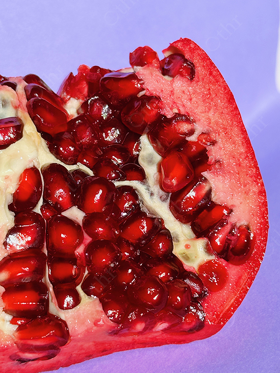 Tight Close-Up of Pomegranate Segment Showing Glossy Red Seeds on Purple Background