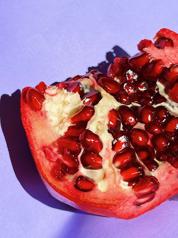 Close-Up of Cut Pomegranate With Glossy Red Seeds Casting Shadow on Purple Background