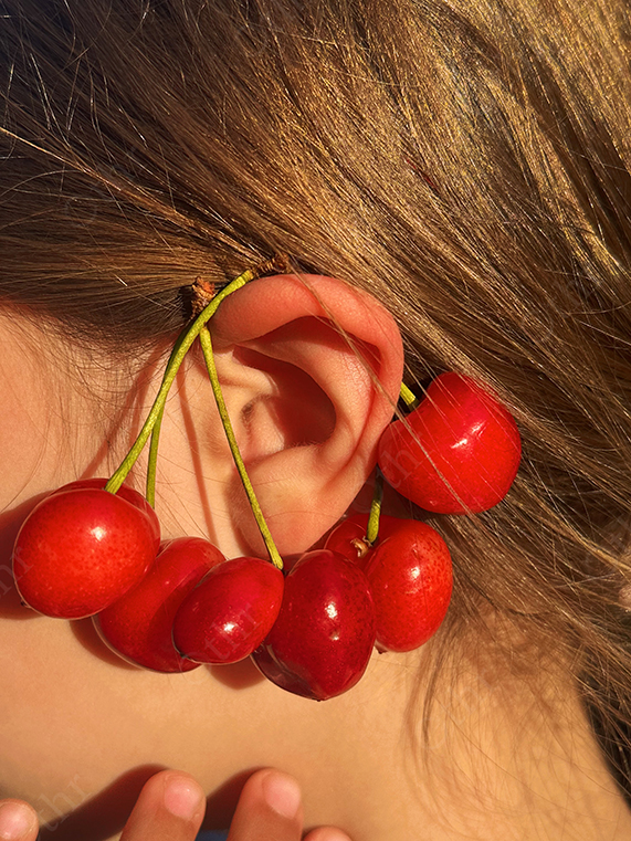 Close-Up of Ear Adorned With Red Cherries Styled as Natural Jewellery in Sunlight