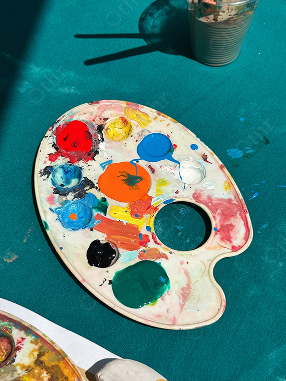 Artist Paint Palette With Mixed Acrylic Colours on Teal Fabric Surface in Sunlight