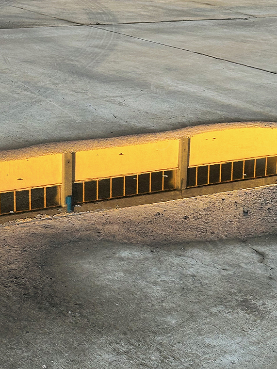 Yellow Curb Edge Casting Long Shadow Across Concrete Pavement in Low Sunlight