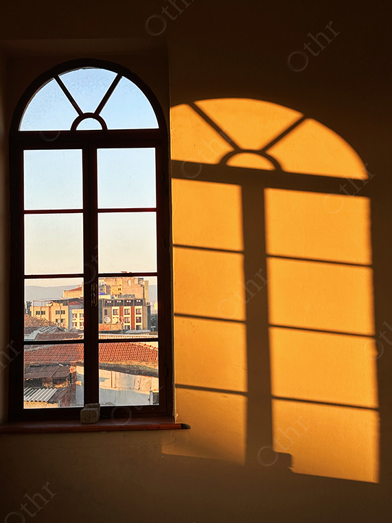 Arched Window Casting Warm Sunlight Shadow on Interior Wall at Golden Hour