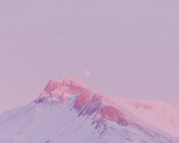 Moonrise over snow covered mountain ridge bathed in soft pink twilight hues.