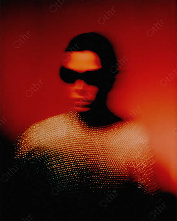 Blurred fashion portrait of woman wearing sunglasses and chainmail top with a red studio background.