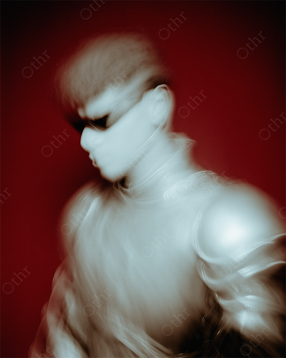 Blurred futuristic armoured figure wearing sunglasses with red studio background.