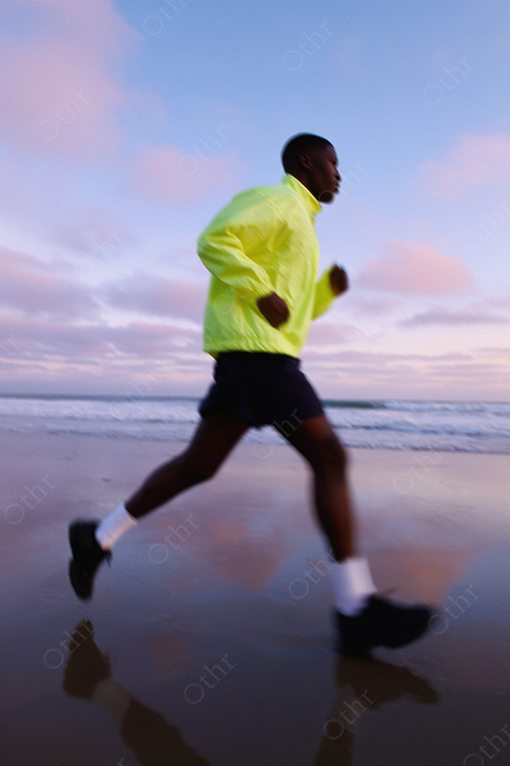 Jogger in neon gear running along beach at sunset