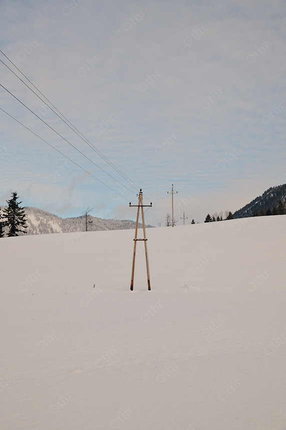 Power Lines Crossing Snow-Covered Field With Distant Hills