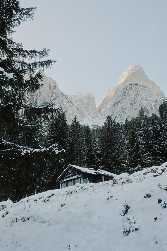 Snow-Covered Wooden Cabin Beneath Jagged Alpine Peaks at First Light