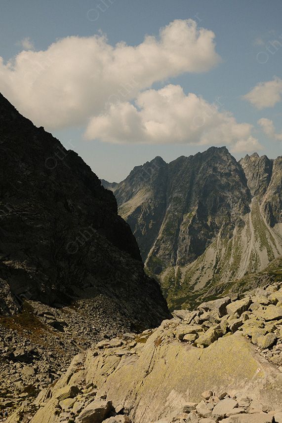 Rocky Mountain Pass Opening to Deep Valley Under Cloudy Blue Sky