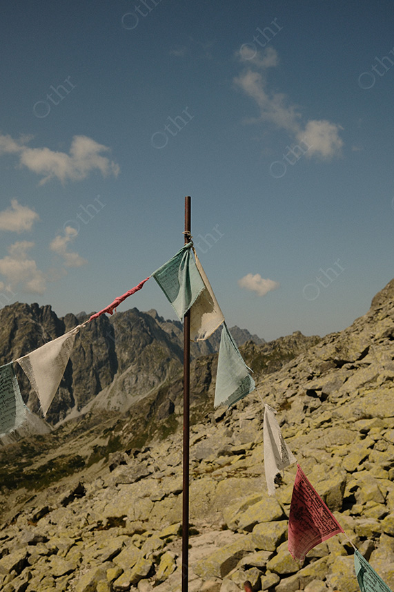 Prayer Flags Hanging from Pole on Rocky Alpine Ridge Under Clear Sky