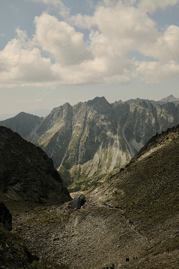 Mountain Hut on Rocky Trail in Alpine Valley Under Large Clouds