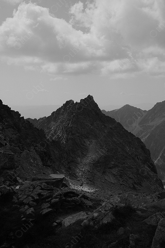 Jagged Mountain Ridge in Dramatic Light Beneath Clouded Sky – Black and White
