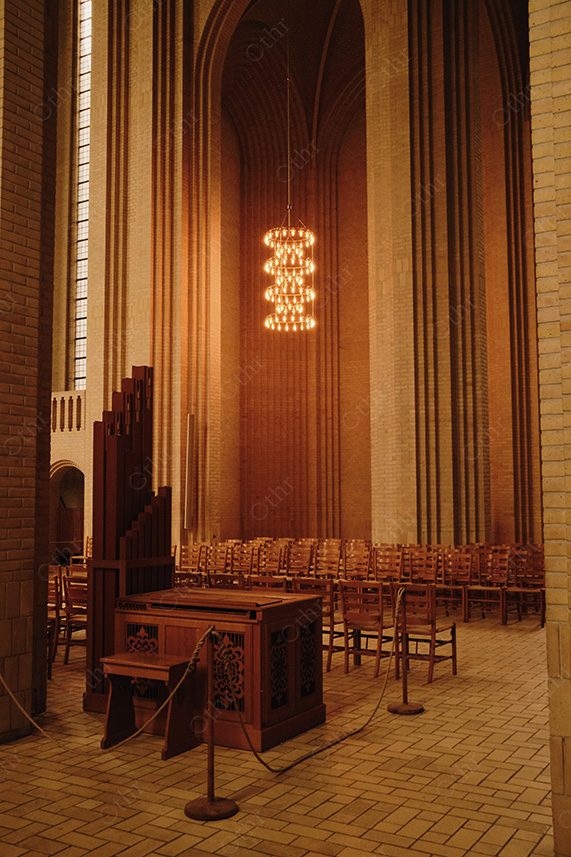 Organ Console and Seating Inside Tall Brick Cathedral Nave Under Warm Light