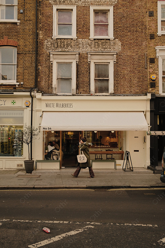 Pedestrian Walking Past Cafe Shopfront on Brick Street in Soft Overcast Light
