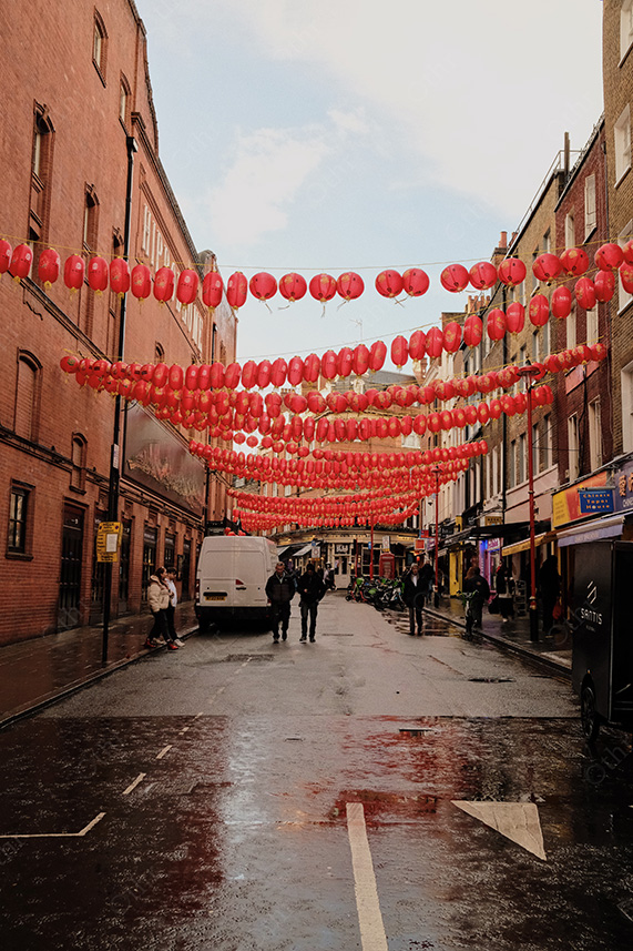 Red Lanterns Strung Across Wet City Street With Reflections and Pedestrians