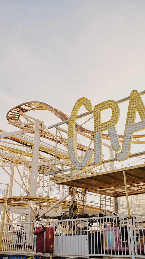 Partial “Crazy” Amusement Ride Sign Framed by Roller Coaster Structure in Warm Daylight