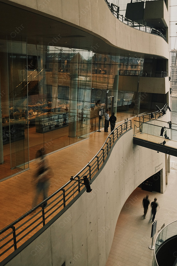 People Walking Along Curved Interior Balcony Inside Modern Concrete and Glass Building