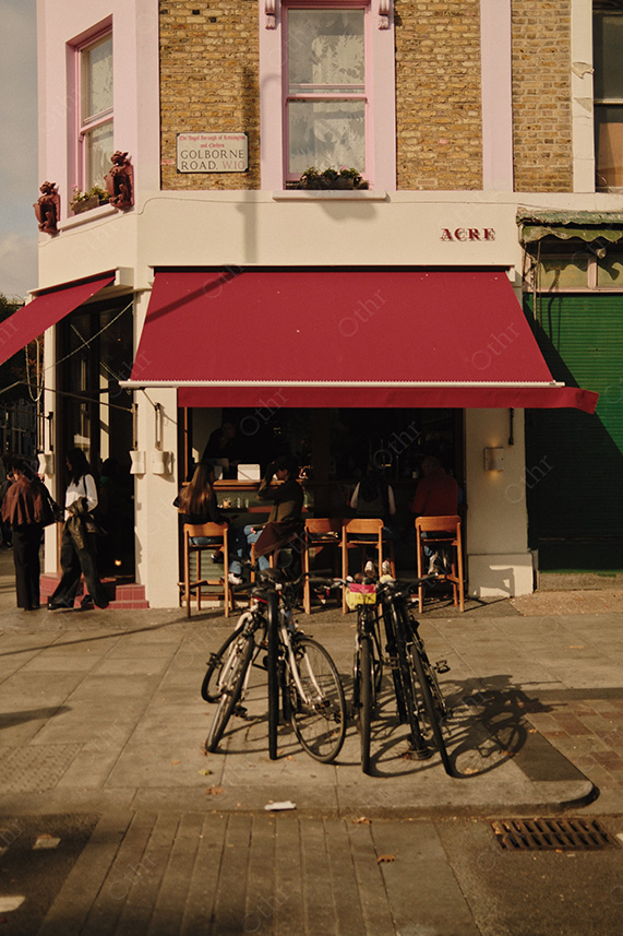 Street Corner Cafe With Red Awning, Outdoor Seating, and Bicycles in Warm Afternoon Light