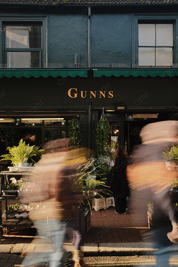 Flower Shopfront With “Gunns” Sign and Pedestrians in Motion Blur on Narrow Street