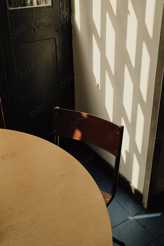 Wooden Chair and Round Table in Sunlight With Window Shadows on White Wall
