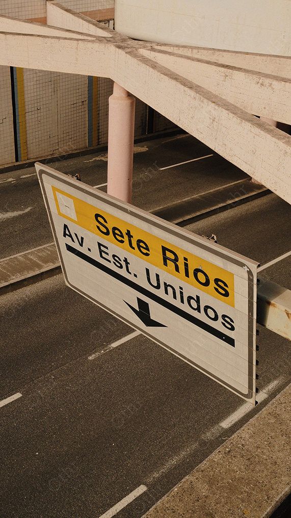Road Sign Reading “Sete Rios Av. Est. Unidos” Above Empty Lanes in Warm Sunlight