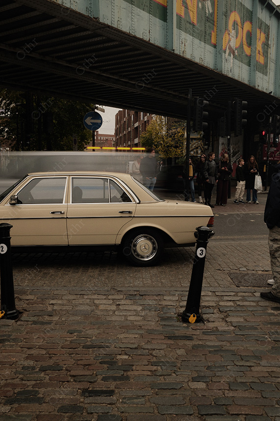 Vintage Saloon Car Parked Under Steel Railway Bridge With Pedestrians on City Footpath