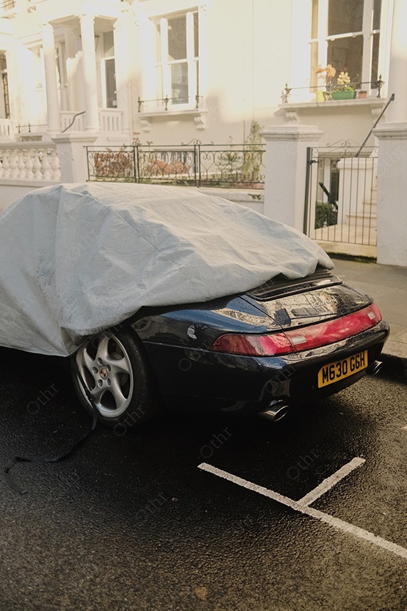 Covered Sports Car Parked on Wet Street With Reflections in Bright Daylight