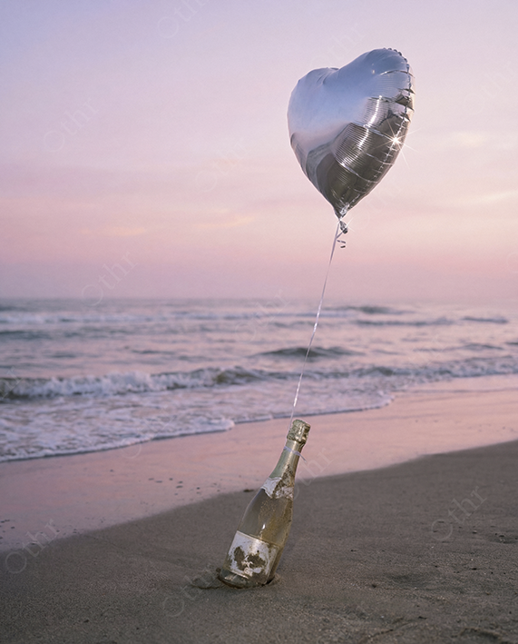 Silver Heart Balloon Tied to Bottle on Sandy Beach at Sunset