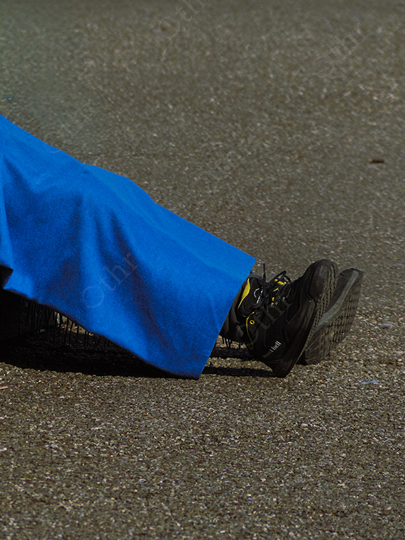 Black Trainers Partially Covered by Blue Fabric on Sunlit Asphalt Surface
