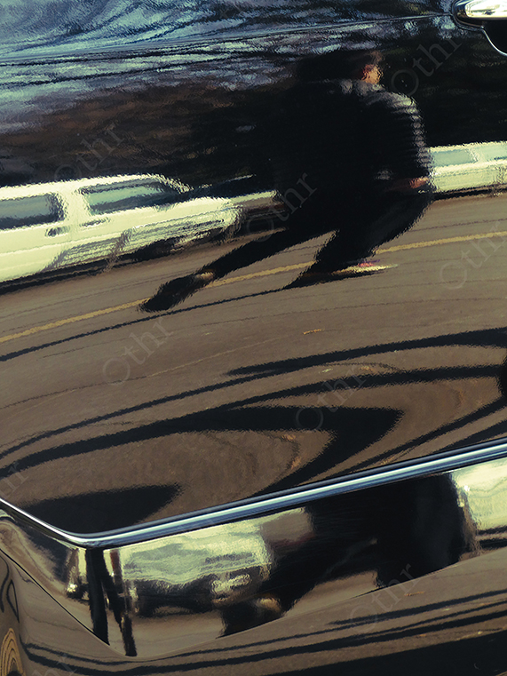 Distorted Reflection of Pedestrian and Parked Cars on Glossy Black Vehicle Surface
