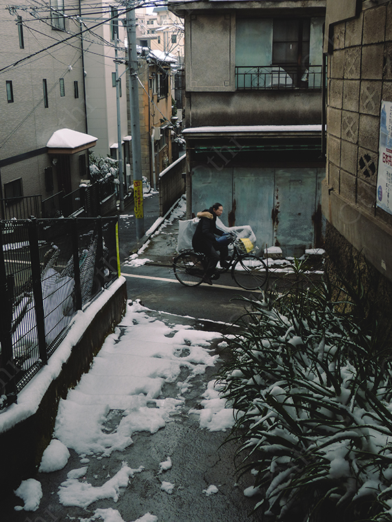 Person Riding Bicycle Through Snow-Covered Narrow Residential Street