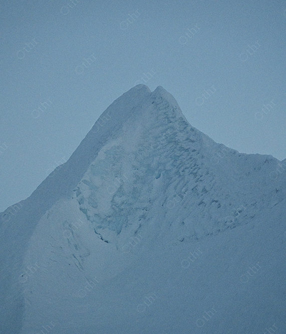 Snow Covered Mountain Peak Emerging Through Mist Under Pale Blue Sky