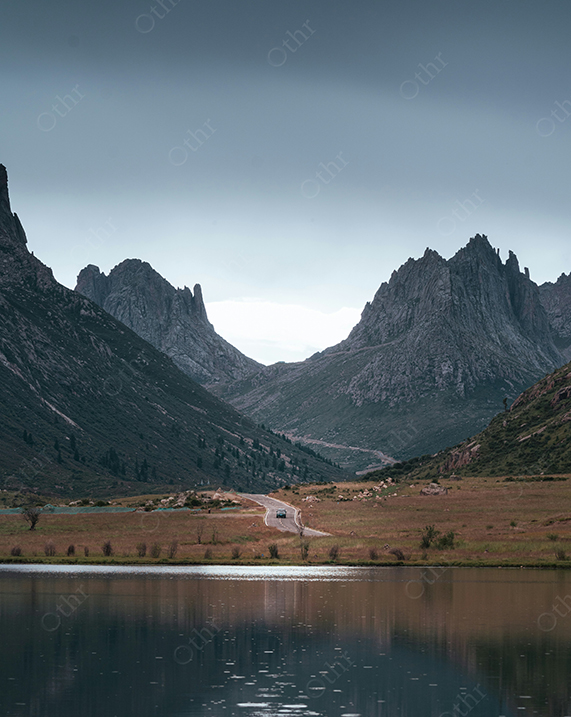 Winding Road Through Valley Between Rocky Mountains Reflected in Calm Lake