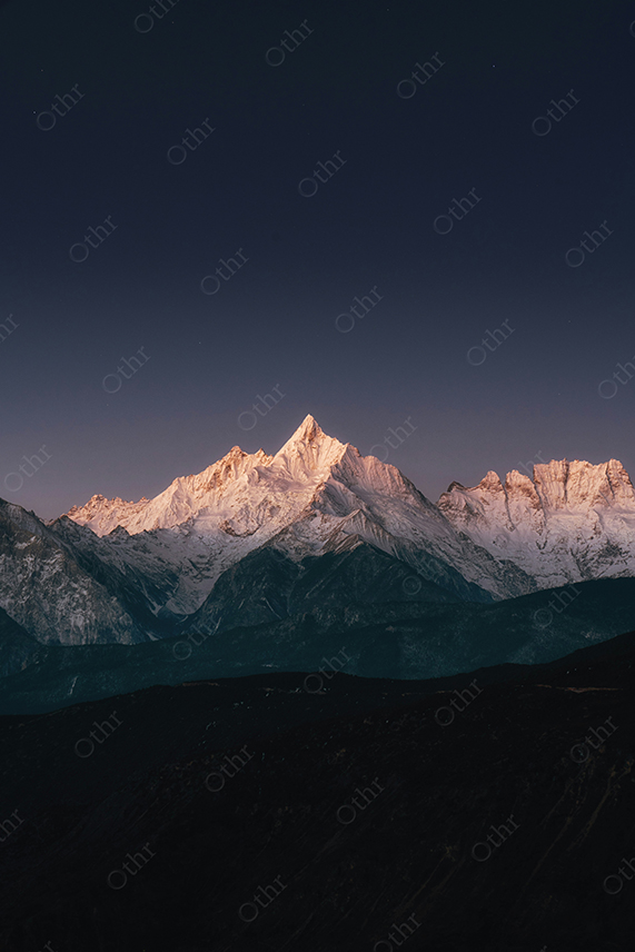 Snow Covered Mountain Peaks Lit by Soft Light Under Clear Night Sky