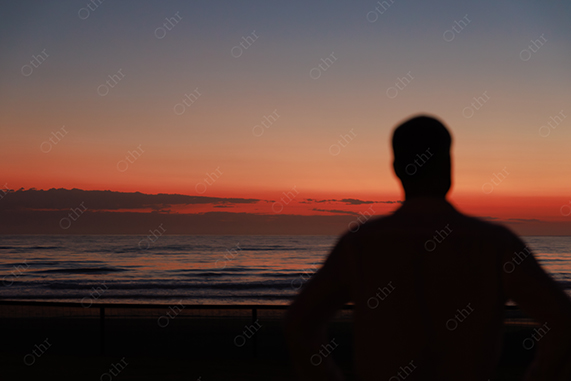 Silhouette of Person Standing by Ocean at Sunset With Orange Horizon and Calm Waves