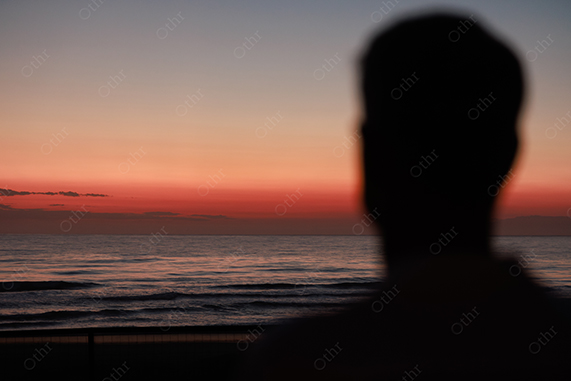Out-of-Focus Silhouette of Person Facing Ocean at Sunset With Orange Gradient Sky