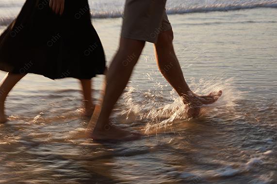 Close-Up of Couple Walking Through Shallow Water With Splashes at Beach