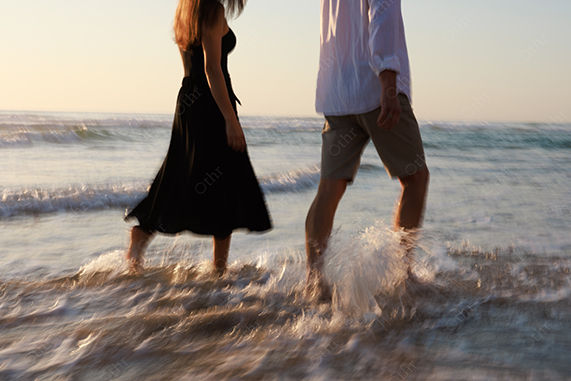 Couple Walking Along Shoreline With Waves at Sunset in Soft Light